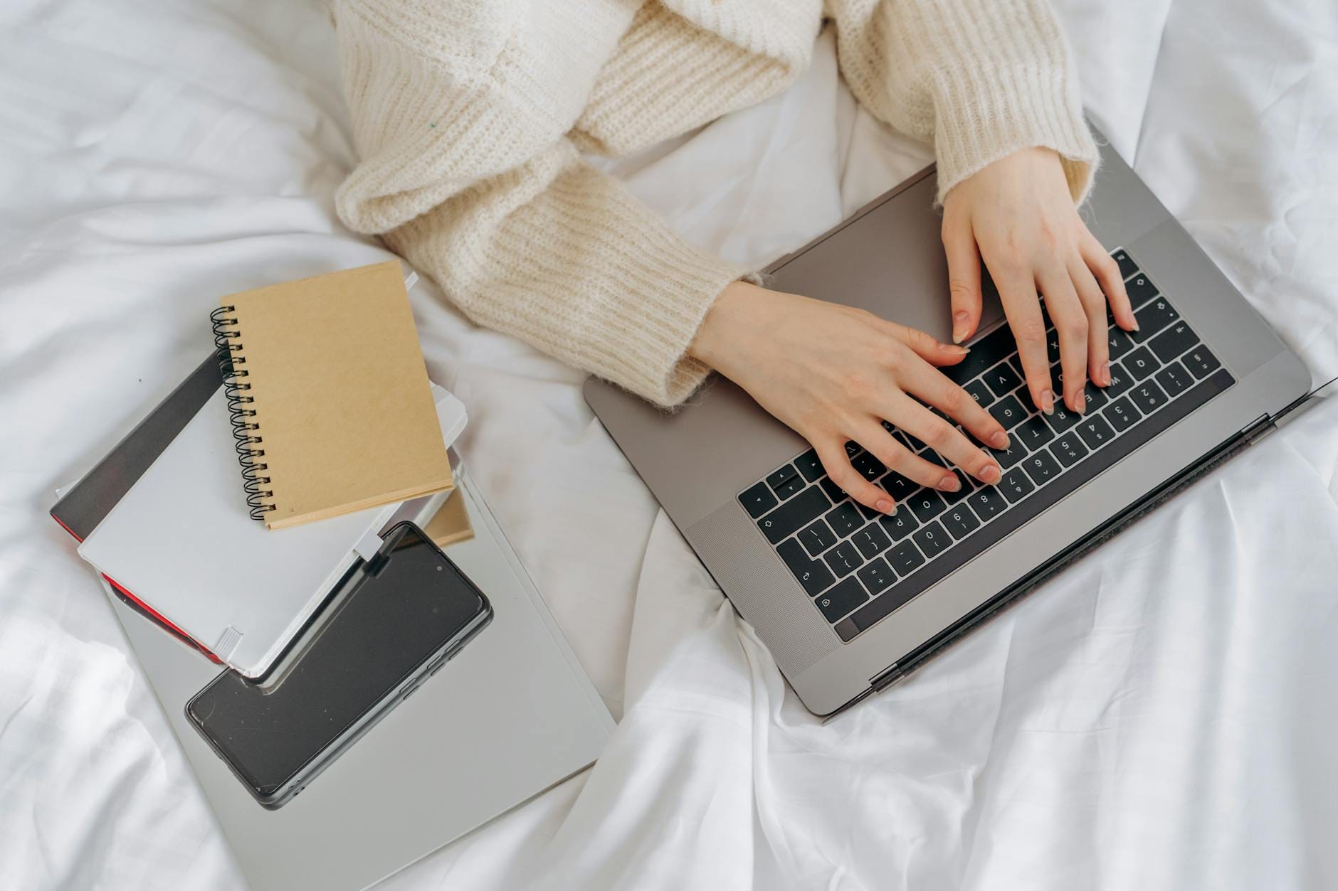 Osoba pisząca na laptopie przy biurku z papierowymi notatkami