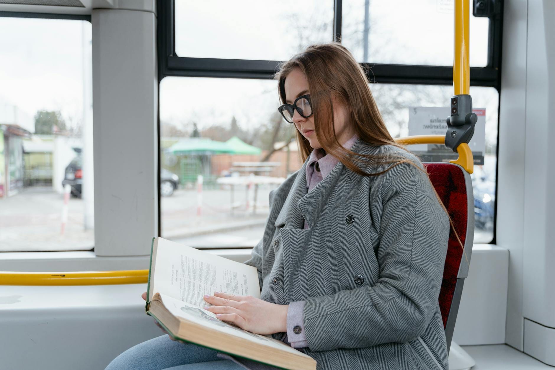 Studentka w okularach czyta książkę w autobusie podczas dojazdu