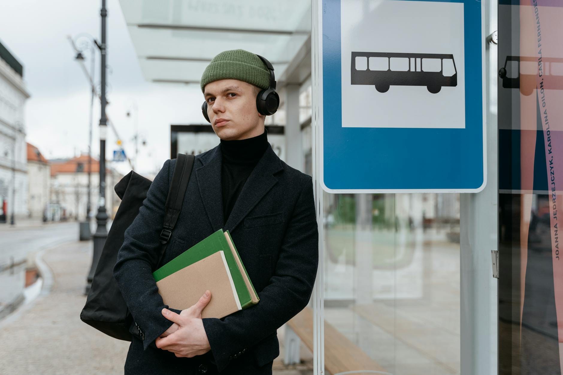 Uczeń z książkami i słuchawkami czeka na autobus w mieście