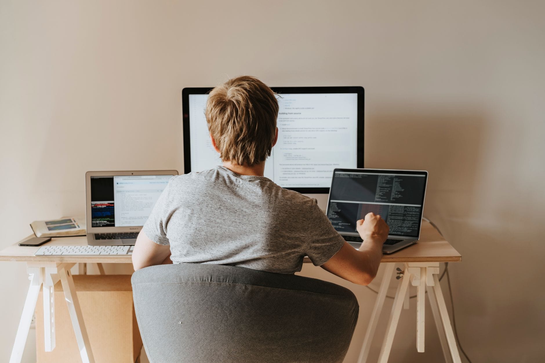 Nastolatek programuje na kilku laptopach w nowoczesnym biurze