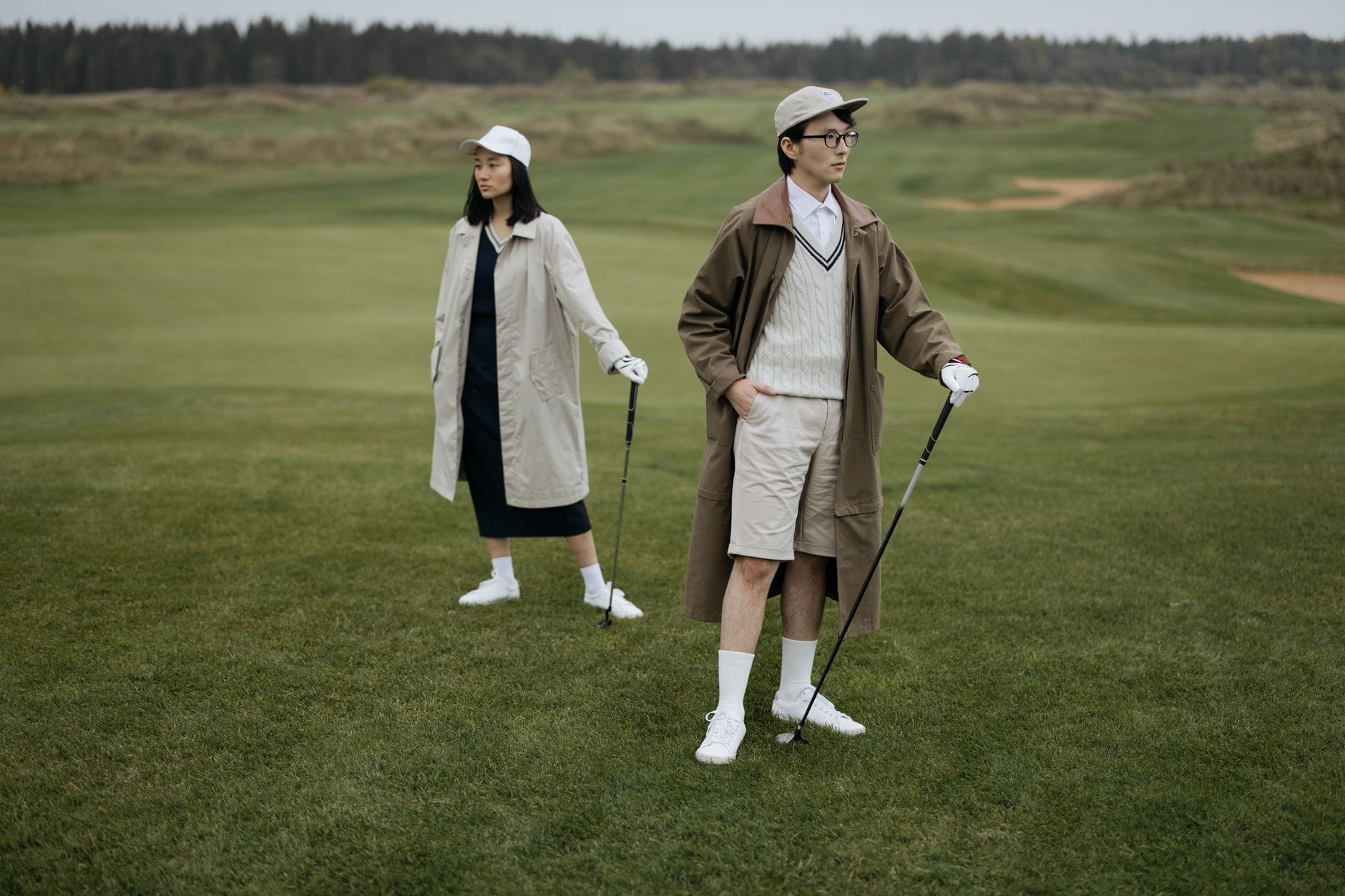 Para młodych golfistów w modnych płaszczach na zielonym polu golfowym