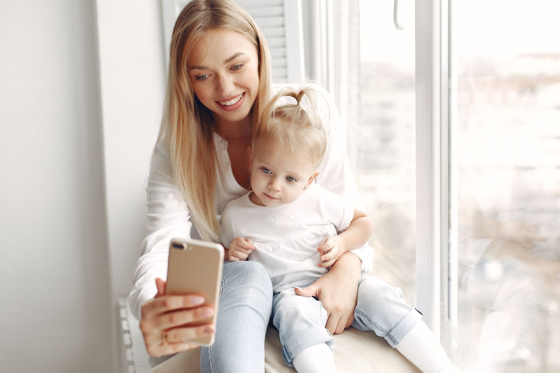 Mama z córką przy oknie wspólnie patrzą na smartfon