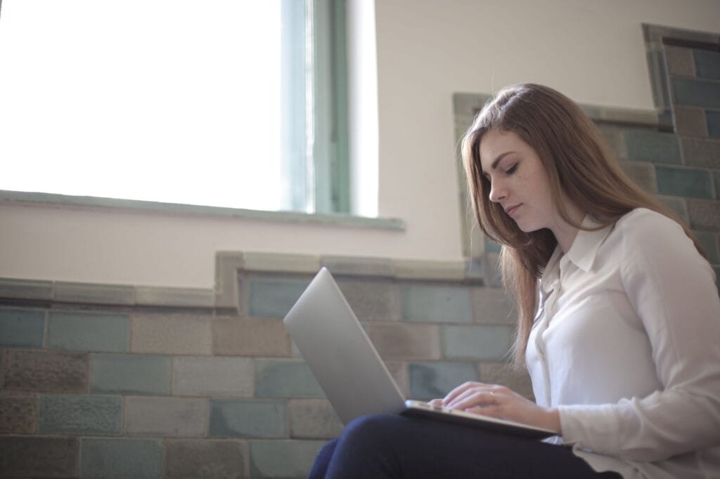 Kobieta w białej koszuli pracująca na laptopie w pomieszczeniu